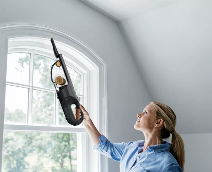 A person using a handheld vacuum to clean a window frame at home.