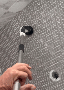 a gif showing the reviewer using a long-handled cleaning tool to scrub a shower floor with gray tiles
