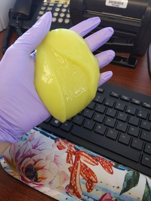 A hand holding the yellow cleaning gel next to a keyboard