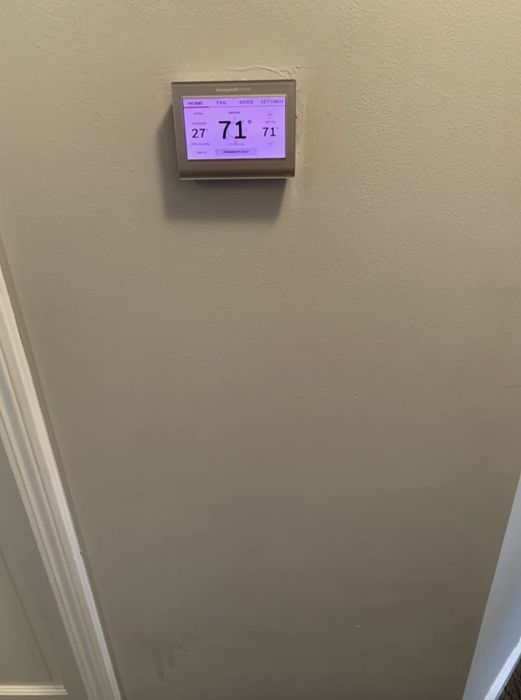 A digital thermostat mounted on a wall displays the current temperature as 71°F, with the system programmed to maintain this setting.