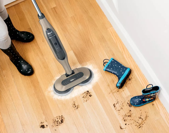 A steam mop removes muddy boot prints from a wooden floor, demonstrating its superior stain-removal capabilities compared to traditional mops.