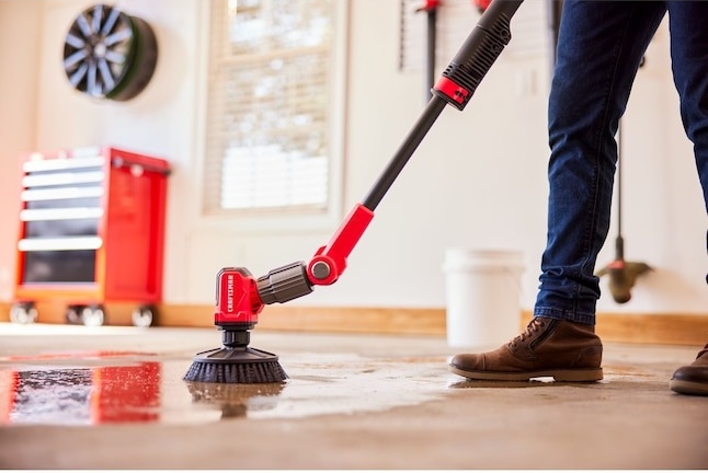 A person using a motorized scrub brush to clean a wet garage floor, showcasing the cleaning tool in action.