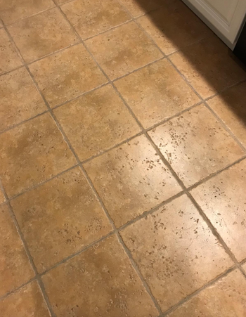 A tiled kitchen floor with light brown tiles and prominent grout lines