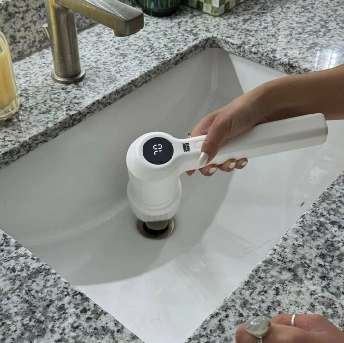 A person grips the power scrubber, using it to clean a bathroom sink.