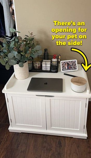 The litter box enclosure in white, serving as a nightstand for a reviewer, with a label that reads: