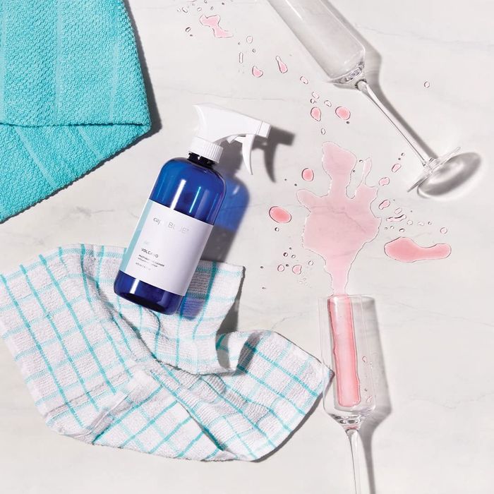 A blue spray bottle placed next to a spilled glass of pink liquid.