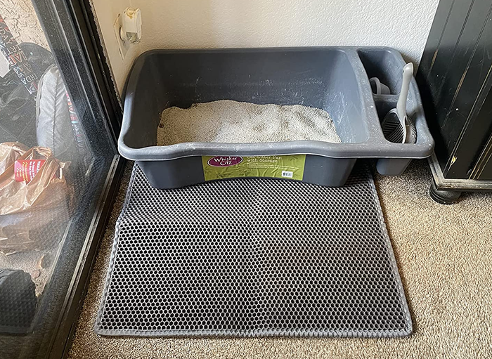A reviewer's photo showing a litter box placed on a gray honeycomb-patterned mat.