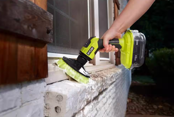 A person cleans a window ledge using the Ryobi power scrubber.