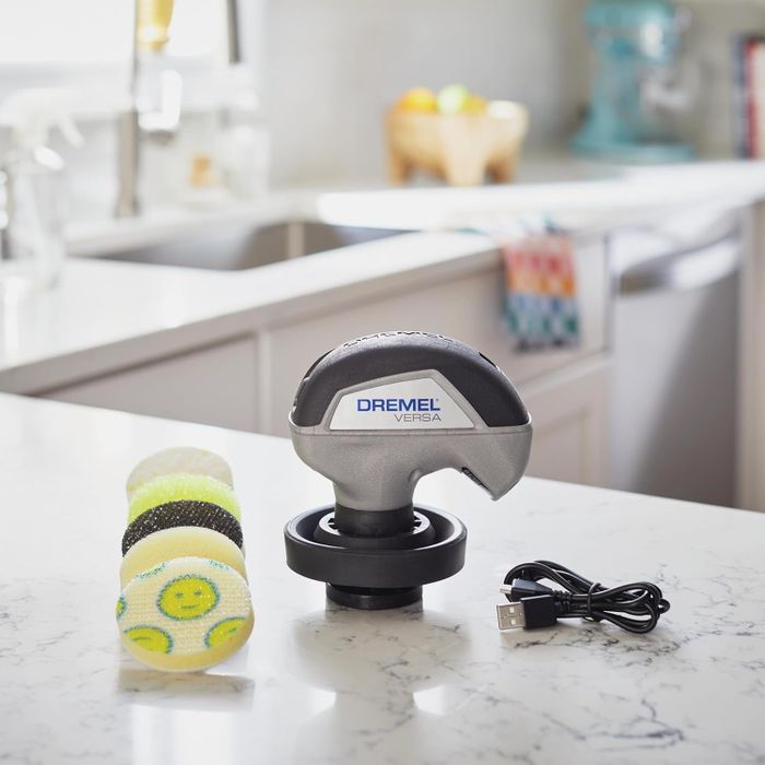 The Dremel Versa cleaning tool sits on a kitchen counter, with its interchangeable pads and USB charger, ready for various cleaning tasks.