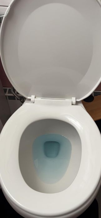 Overhead view of a pristine, open toilet with a white lid and blue water swirling in the bowl
