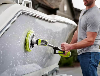 A person uses an electric scrubber to clean a boat hull, removing soap and grime.