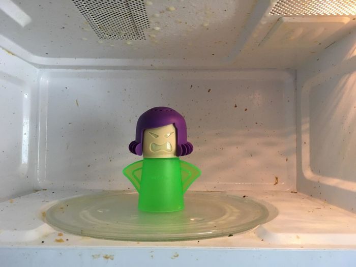 A human-shaped steam cleaner placed inside a grimy microwave.