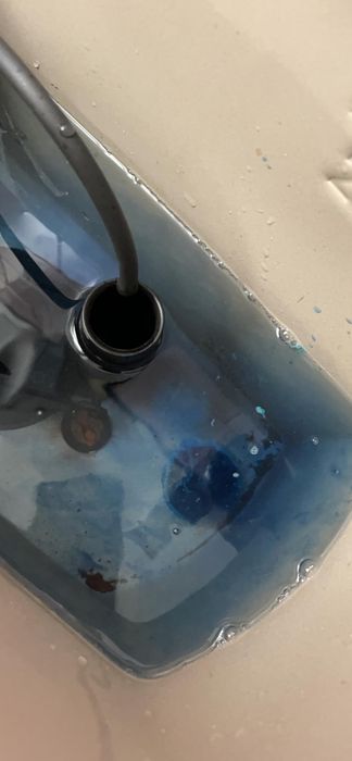 Close-up shot of a sink featuring a black tube inside, draining a cloudy blue liquid