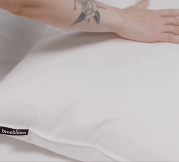 A gif showing a model testing the firmness of a pillow by pressing down on it