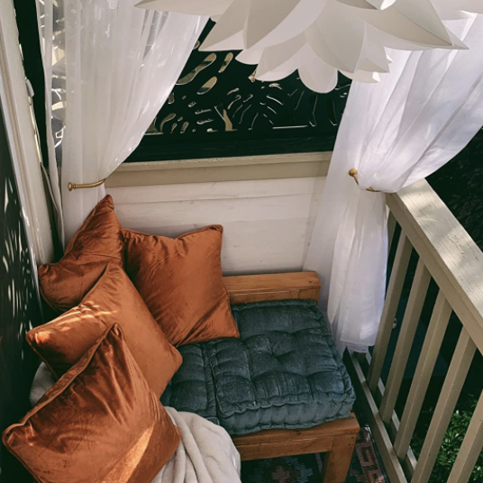 A reviewer's covered deck adorned with several pillows and a cushion resting on a wooden stool