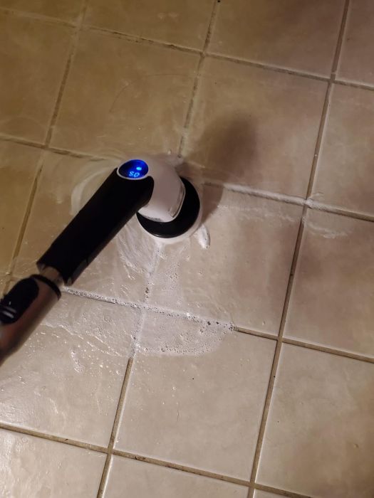 Reviewer using an electric scrub brush to clean a tiled floor with foam