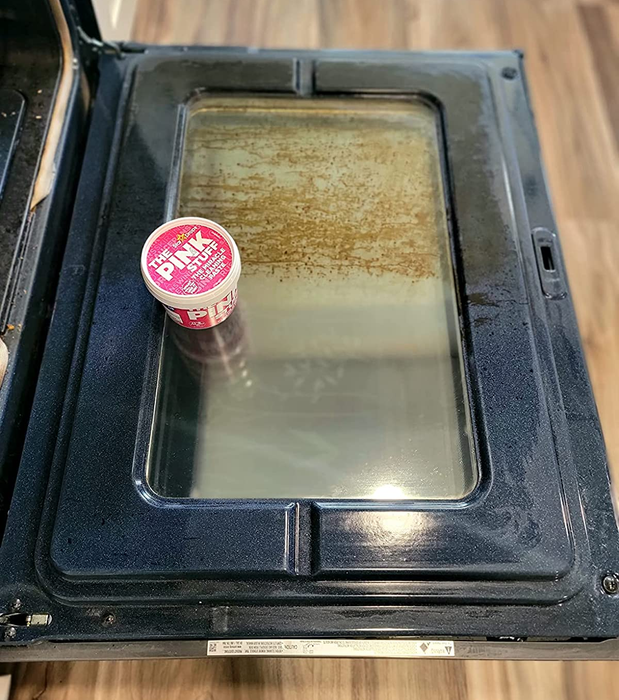 Reviewer photo showing a tub of The Pink Stuff on an oven door, half dirty and half clean