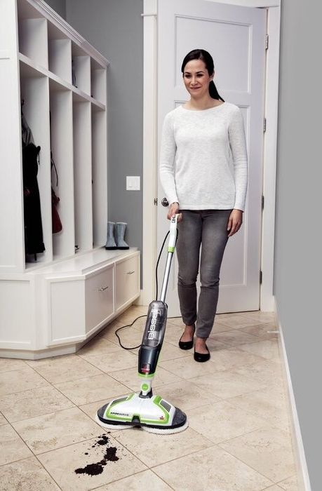 A person is using a Bissell SpinWave floor cleaner on a tiled surface to tackle a dirt stain.