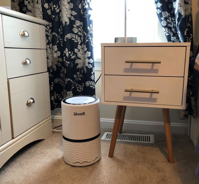 A white air purifier placed beside a nightstand