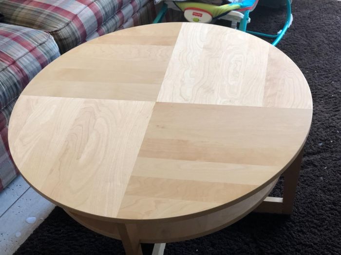 Round wooden coffee table on a patterned rug beside a plaid sofa and a baby chair