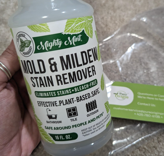 Hand holding a bottle of Pure Origin Mighty Mint Mold & Mildew Stain Remover