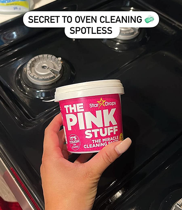 Reviewer holding a tub of The Pink Stuff over their freshly cleaned stove with the text: secret to oven cleaning, spotless