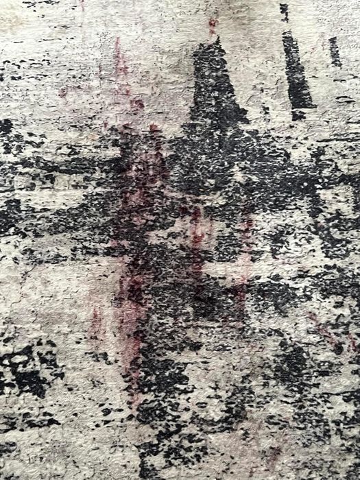 A close-up view of a distressed, abstract rug with a noticeable dark red stain.