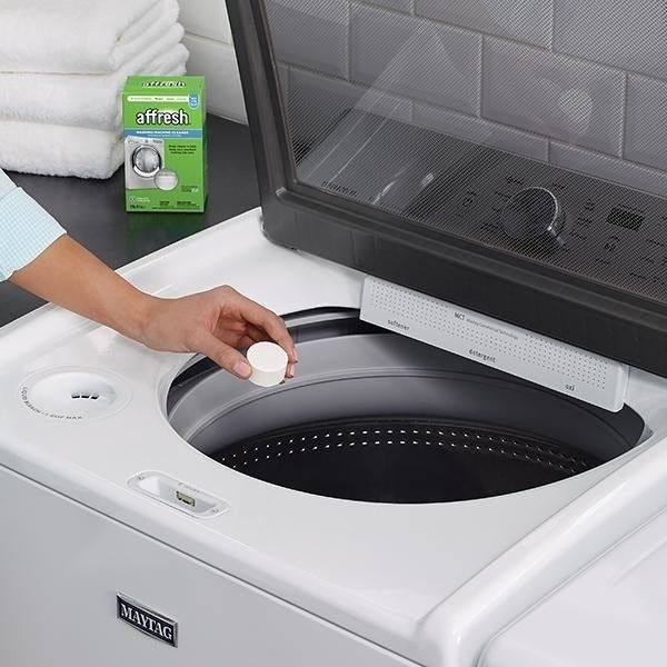 A model's hand dropping a tablet, roughly the size of a quarter, into a washing machine.