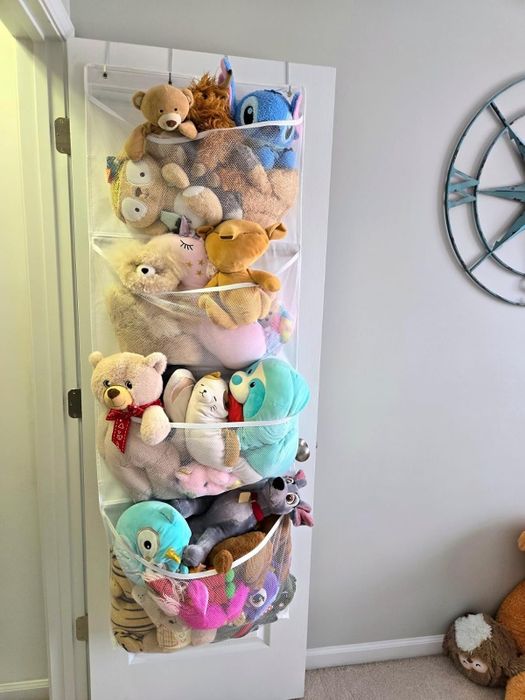A white door adorned with mesh organizers filled with a collection of stuffed animals, from bears and unicorns to beloved characters like Stitch and Olaf. A globe wall decoration adds a whimsical touch.