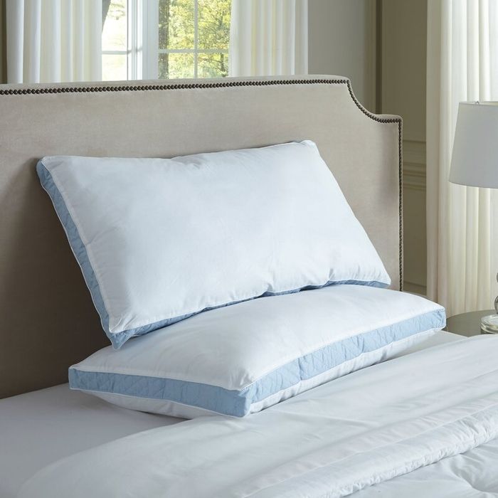 A neatly made bed showcases two plush pillows with light trim, complemented by an upholstered headboard in a bright, spacious bedroom
