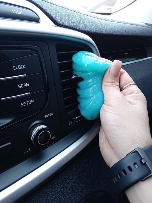 Hand pressing blue cleaning gel into a car’s air vent