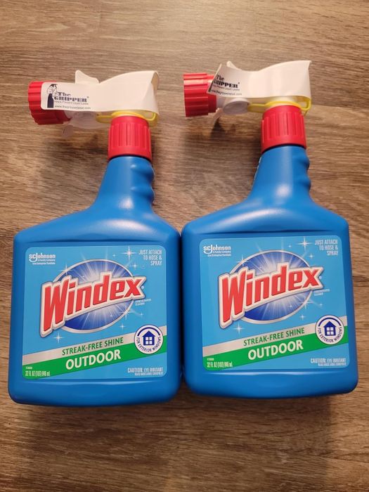Two bottles of Windex Outdoor spray cleaner, featuring a streak-free shine formula, displayed on a wooden surface.