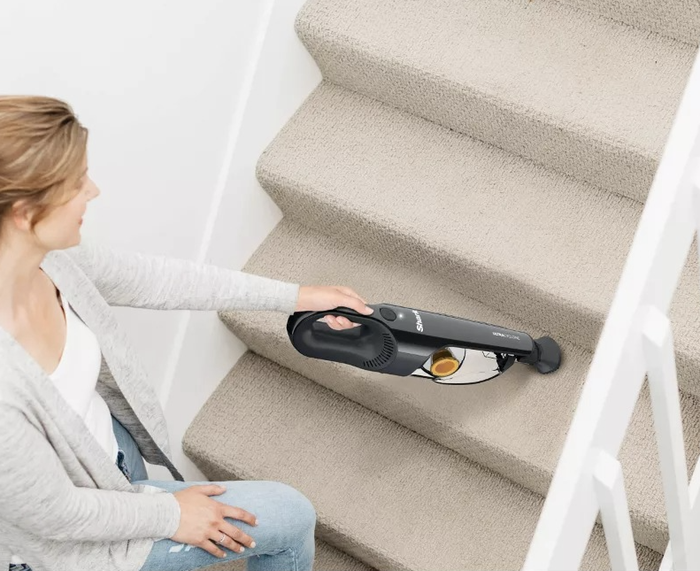 A person using a handheld vacuum to clean carpeted stairs.