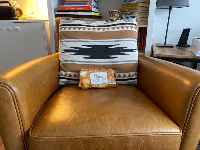 A pack of 3-in-1 leather wipes resting on a leather armchair with a decorative pillow in the background