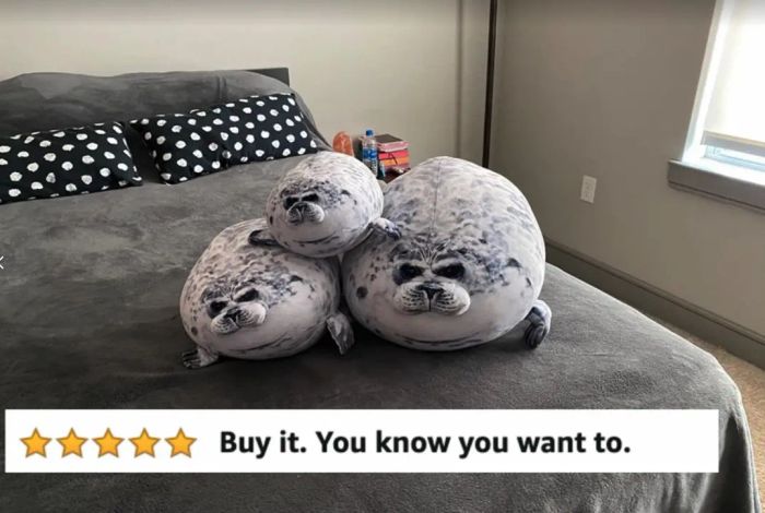 A reviewer's photo showing the seal pillows in three different sizes spread out on a cozy grey bed
