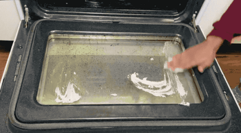 Someone applying the scrub to a grimy oven door