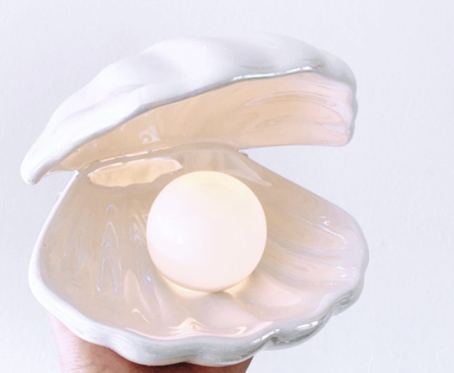 A hand holding the iridescent shell lamp with a glowing pearl light inside