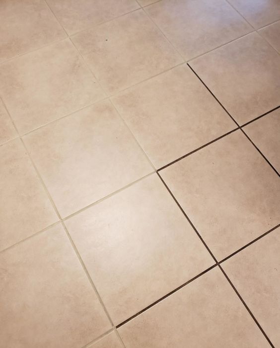 A reviewer's photo displaying a tiled floor with one half showing dirty grout and the other half revealing clean, white grout after using the pen