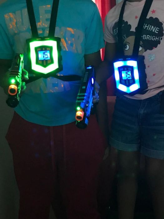 A reviewer's photo showing two individuals wearing glowing vests and holding illuminated laser guns