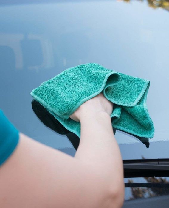 A model cleaning a car windshield with a microfiber cloth