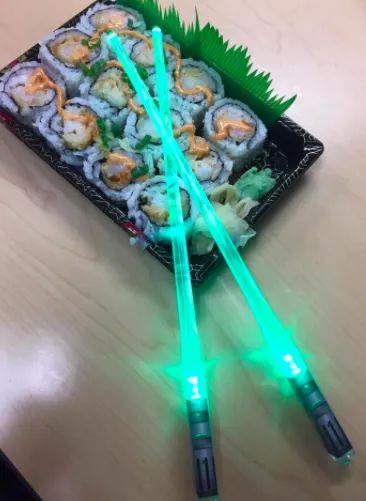 Green lightsaber chopsticks resting on a tray filled with spicy crab sushi rolls
