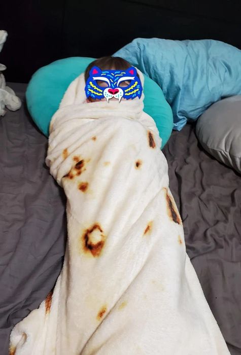 A reviewer's photo of their child wrapped up like a burrito in the tortilla blanket