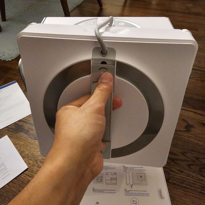 A person holding a sleek, rectangular kitchen appliance featuring a built-in handle, surrounded by instruction manuals and paperwork