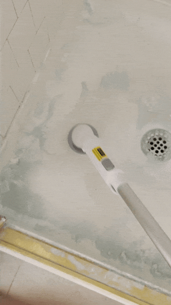 A reviewer uses the spin scrubber to clean the shower floor.