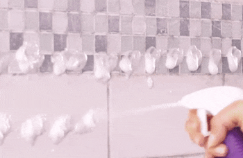 A model spraying the foam onto a dirty shower surface, followed by wiping it clean for a fresh shine.