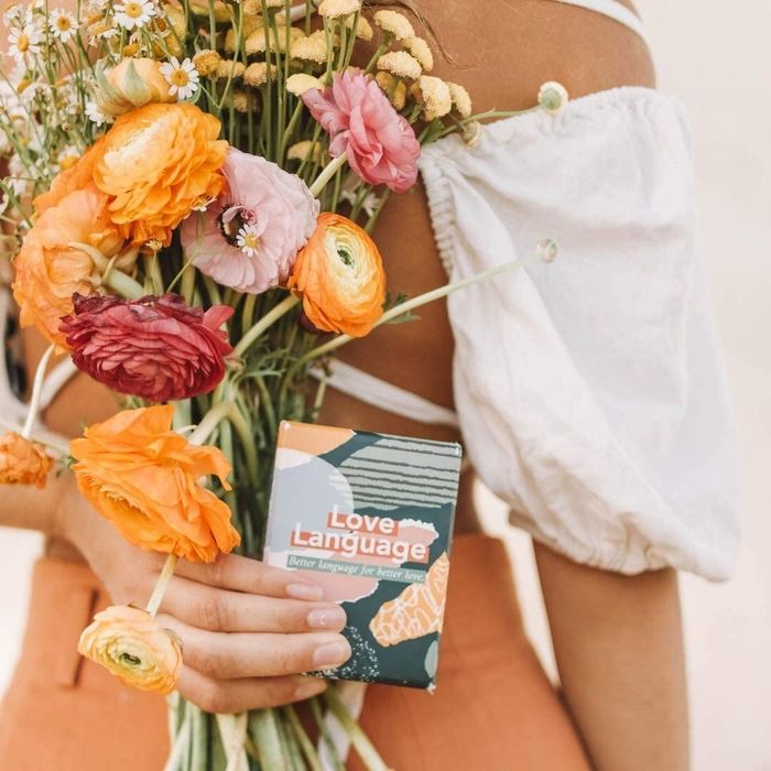 A person holding a card game box along with a bouquet
