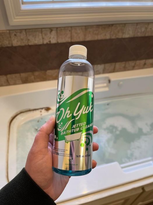 A reviewer is seen holding up a bottle of tub cleaner above their tub.