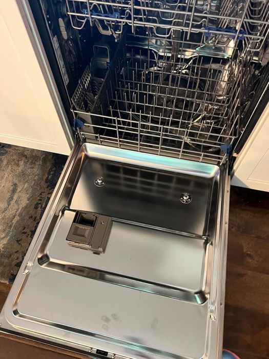 A stainless steel dishwasher with its door open, showing an empty top rack and the detergent compartment inside the door