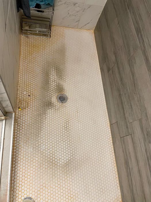 A reviewer’s photo showing a dirty tile shower with hard water stains on one side, and the other side perfectly clean after using the cleaner