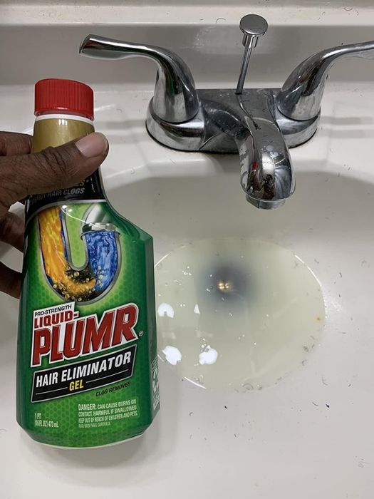 a reviewer holds a bottle of Liquid Plumr beside a clogged drain